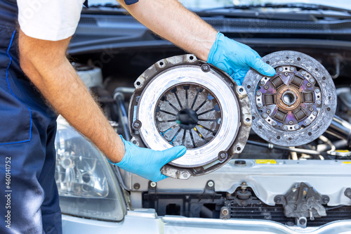 Automotive technician holding used car pressure plate and clutch disc in front of the vehicle engine photo