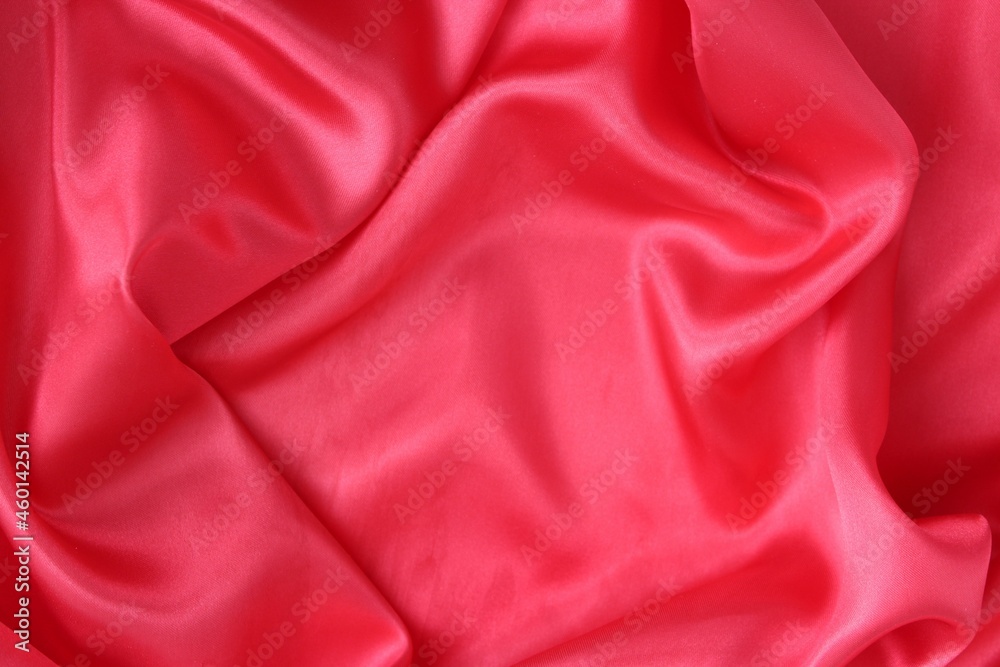 Fototapeta premium Delicate red fabric with beautiful pleats. Silk, satin are folded freely. It can serve as a background for the inscription.