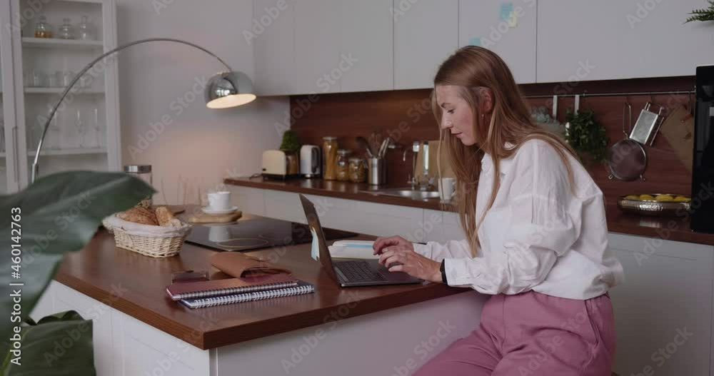 Beautiful relaxed Caucasian business woman using laptop to work online at luxury home kitchen table. Workaholic concept. Beautiful relaxed Caucasian business woman using laptop to work online at luxury home kitchen table. Workaholic concept.