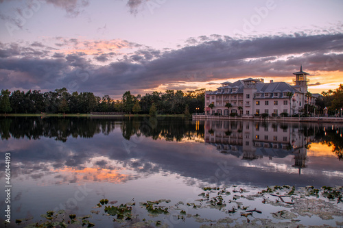 A hotel in Celebration (Orlando, Kissimmee), Florida reflects at the edge of a small lake during sunset with interesting cloud formations above. photo