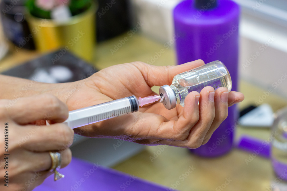 Señora sosteniendo una jeringa sacando liquido de un frasco de medicina para el cabello en un salon profesional de belleza