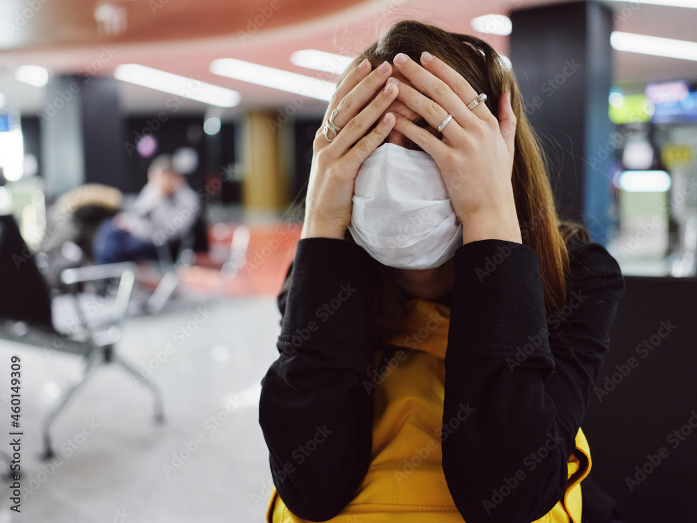 Fototapeta premium woman in medical mask covers her face with her hands fatigue flight delay airport
