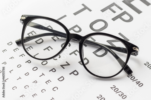 Eyeglasses with black frame on visual test chart isolated on white. Eyesight, healthcare and medicine concept.