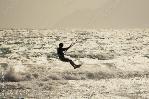 Silhouette of a kite surfer making small jumps over small waves