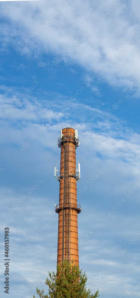 An old red brick factory chimney with various modern antennas for the Internet and mobile communications against cloudy sky.