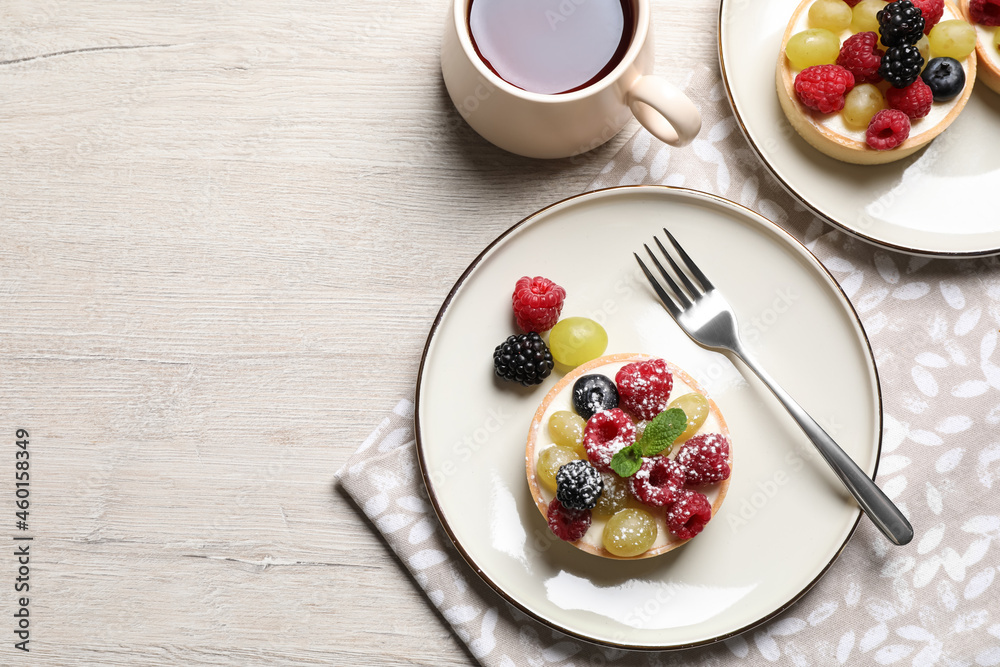Delicious tartlets with berries and tea on light wooden table, flat lay. Space for text