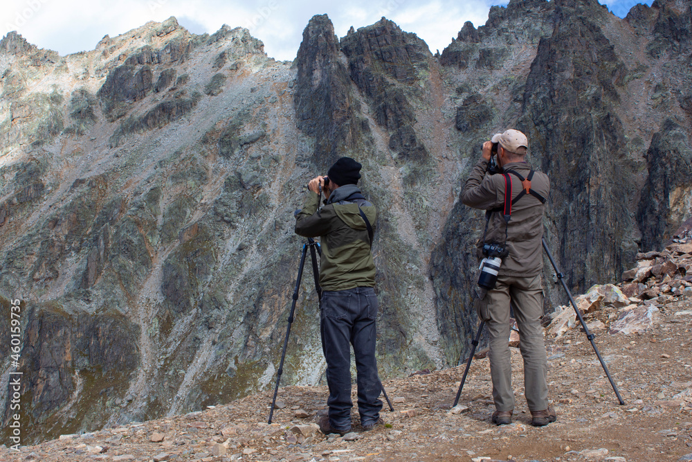 Professional photographers shooting shooting high in the mountains. Two men with photographic equipment stand on a rock.