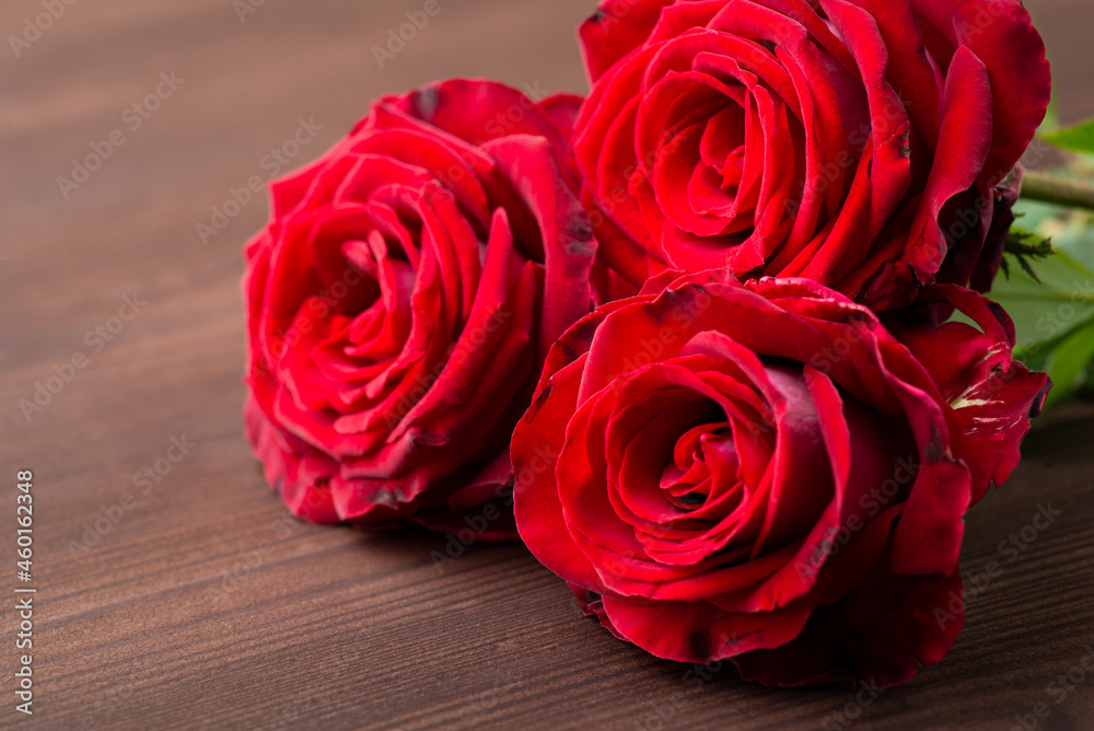 Three red roses in full bloom on dark wooden table. Close-up of small bouquet of roses Three red roses in full bloom on dark wooden table. Close-up of small bouquet of roses