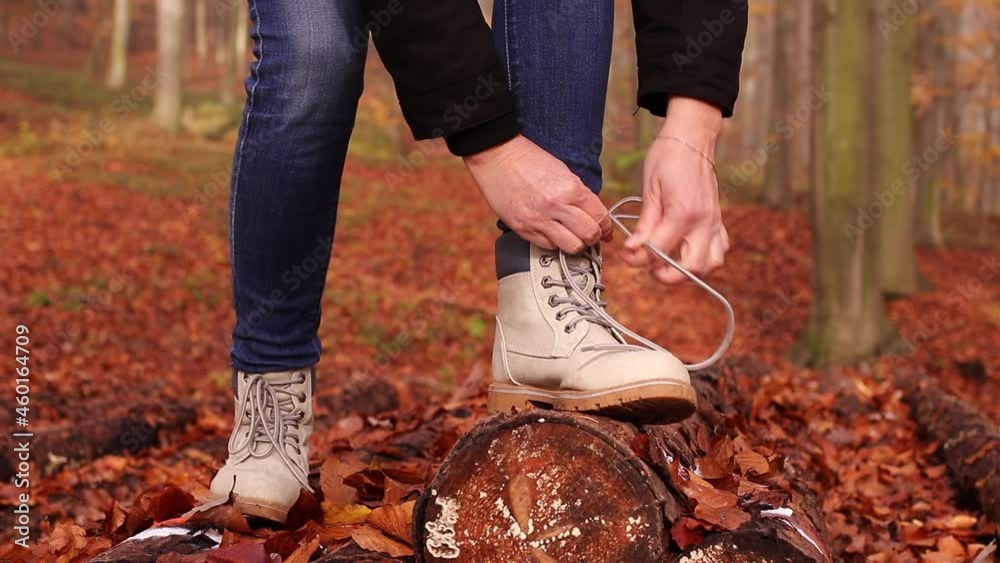 Woman tying shoelace on her hiking boot. Tourist is getting ready for autumn hike at forest trekking trail