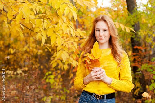 Autumn. red-haired girl in a yellow sweater holds a bouquet of autumn leaves in her hands. Warm tones. Orange. A place for text.