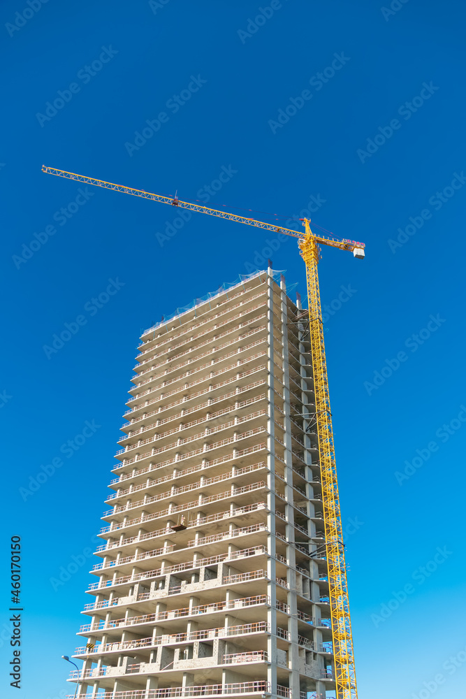 Multi-storey building under construction with a yellow construction crane on a blue sky background with copy space. Vertical photo
