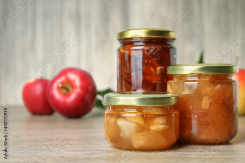 Tasty apple jam in glass jars on wooden table, space for text