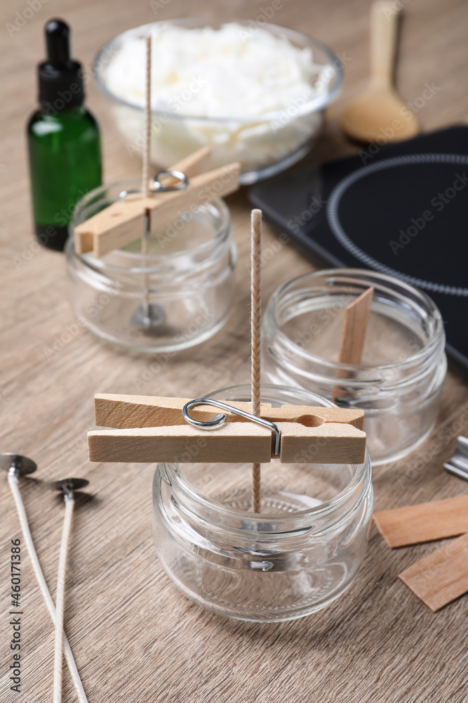 Glass jars with wicks and clothespins as stabilizers on wooden table. Making homemade candles Glass jars with wicks and clothespins as stabilizers on wooden table. Making homemade candles