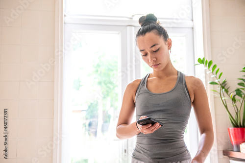 UK, London, Woman in tank top looking at smart phone at home