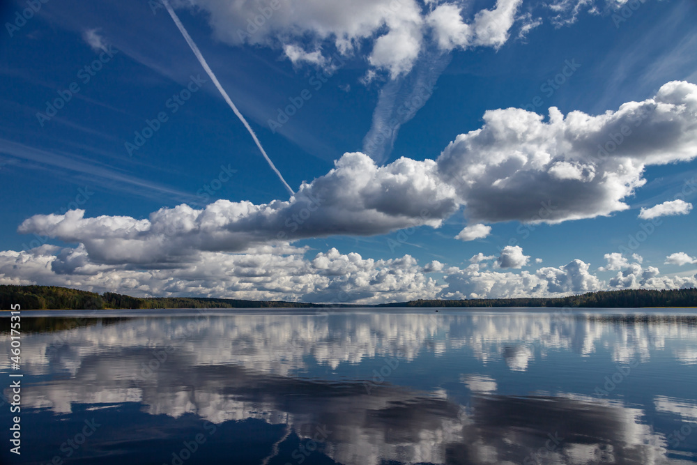 Summer cloudy landscape against the blue sky and its reflection in the water.