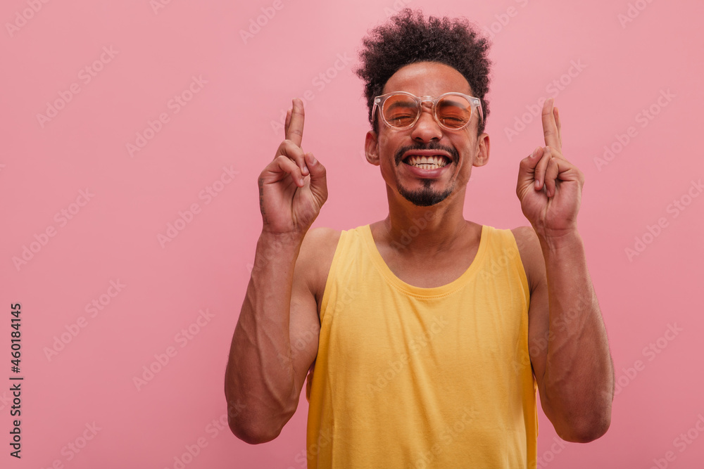 Young African man crosses fingers making wish to win trip for him and beloved wife. Good looking guy with eyes closed in modern glasses and yellow t-shirt strongly believes in fast, happy family trip Young African man crosses fingers making wish to win trip for him and beloved wife. Good looking guy with eyes closed in modern glasses and yellow t-shirt strongly believes in fast, happy family trip