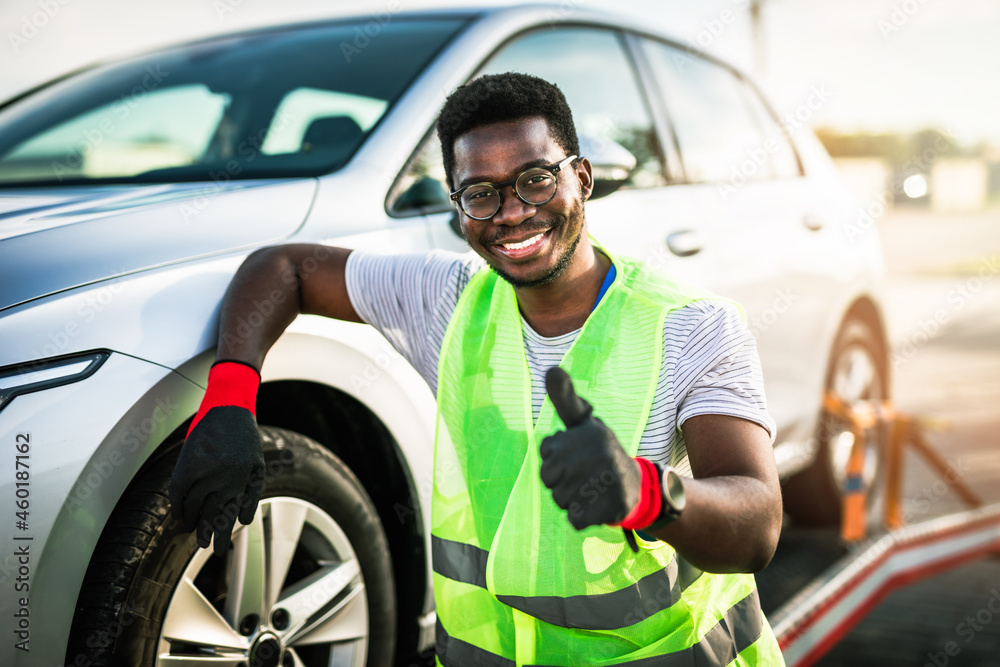 Handsome young African American man working in towing service on the road. Roadside assistance concept. - obrazy, fototapety, plakaty 