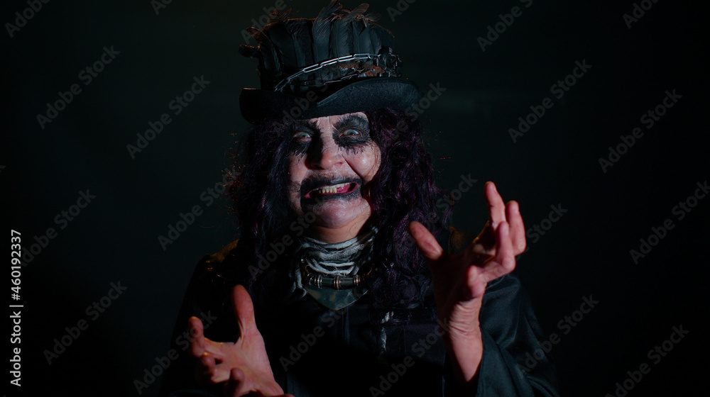 Portrait of sinister senior old mature woman in carnival costume of Halloween witch making faces, trying to scare isolated on black studio background. Horror theme of cosplay clown, vampire, beast Portrait of sinister senior old mature woman in carnival costume of Halloween witch making faces, trying to scare isolated on black studio background. Horror theme of cosplay clown, vampire, beast