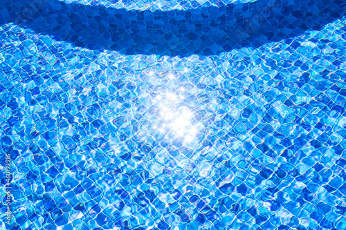 Piscina de vinil em uma residência com estampa de mosaico quadriculado em diversos tons de cor azul. Piscina com degraus internos e reflexo da luz do sol brilhando na água. photo