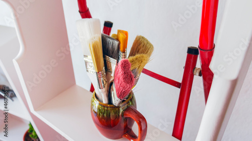 Close-up of a set of colorful brushes in a brown vasel in a bright and white room with natural lighting photo