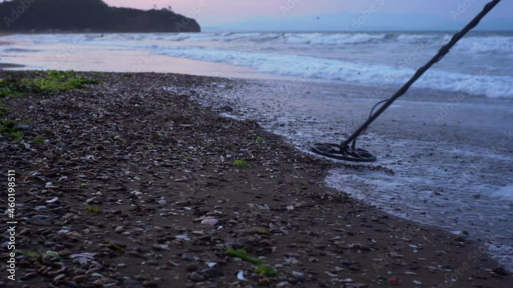 An electronic metal detector and a scoop. A man is looking for the luxuries lost by tourists in water and on the beach. Seaside, foamy waves. Morning An electronic metal detector and a scoop. A man is looking for the luxuries lost by tourists in water and on the beach. Seaside, foamy waves. Morning