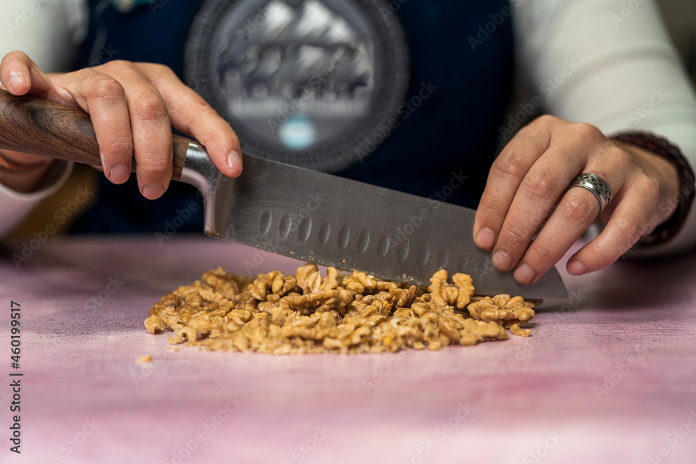 Unrecognizable person using a knife to cut walnuts into small pieces to decorate homemade argentine alfajores