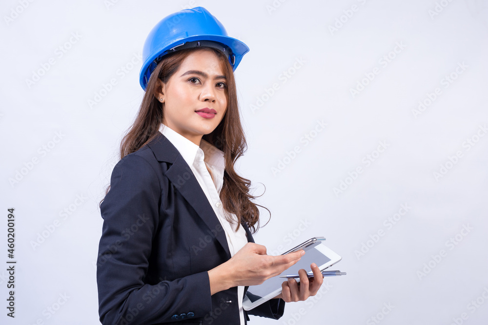 Beautiful Asian female engineer wearing black suit and blue safety helmet using smartphone and laptop computer isolated on gray in the studio background. Beautiful Asian female engineer wearing black suit and blue safety helmet using smartphone and laptop computer isolated on gray in the studio background.