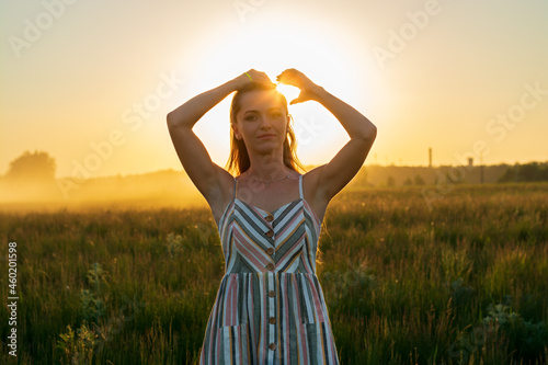 a girl in a dress in a green field in the bright rays of the setting sun.