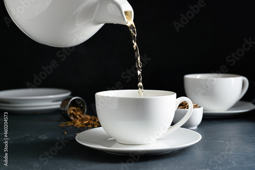 Pouring of tasty hojicha green tea into cup on black background