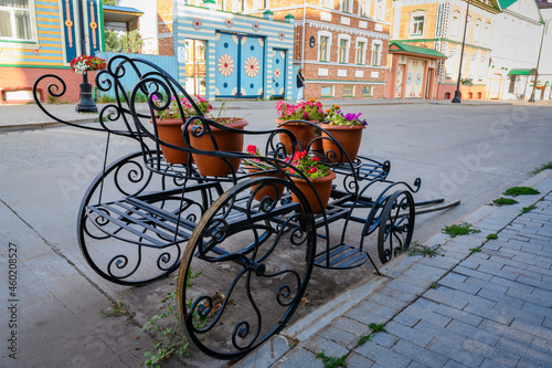 Potted flowers on a wrought iron stand in the form of an old carriage on the street in Kazan, Russia