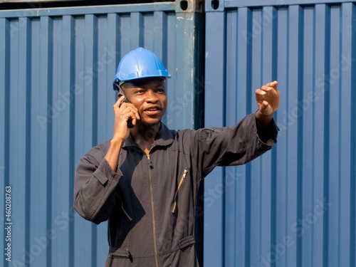 Foreman engineer manager african blue hat black shadow safety talk telephone look pointing finger work report warehouse terminal container import export business customer logistic international