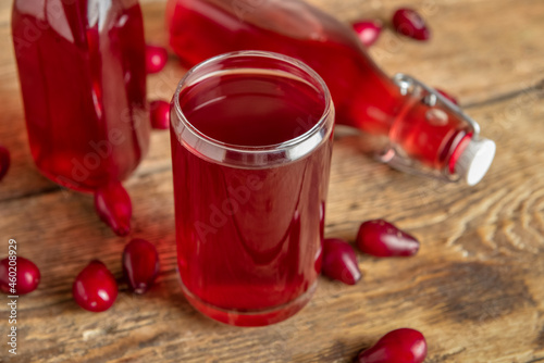 Bottle and glass of fresh dogwood drink on wooden background, closeup photo