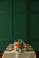 Autumn table setting with fresh pumpkins and flowers near green wall