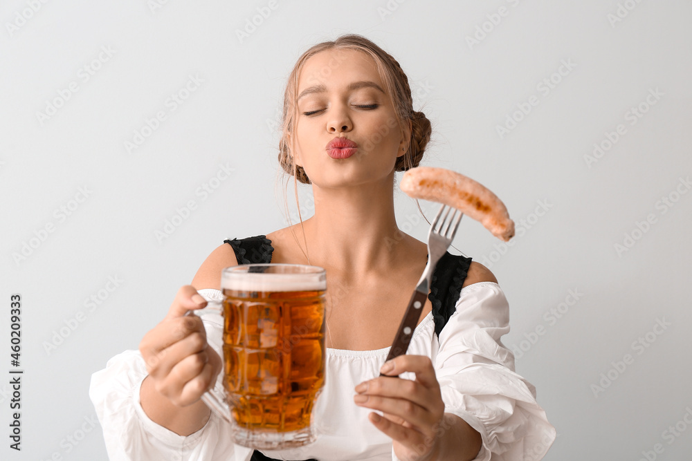 Beautiful woman in traditional German costume, with sausage and mug of beer on grey background Beautiful woman in traditional German costume, with sausage and mug of beer on grey background