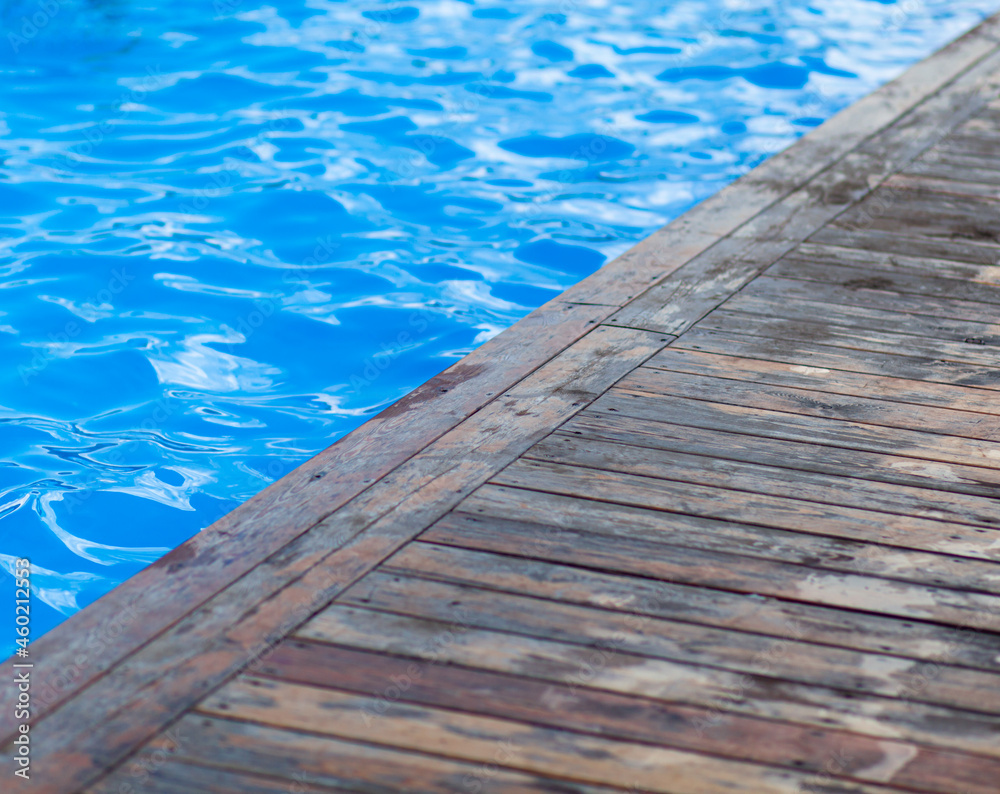 Blue, clear water in an open-air swimming pool. The edges of the pool are made of wood. Water background, ripple and flow with waves. Sea, ocean surface. Overhead top view with place for text.