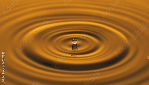 Water drop on water surface with golden light effects background.