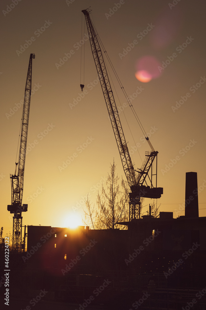 Silhouette of Two Industrial Construction Cranes at Sunset with Lens Flare