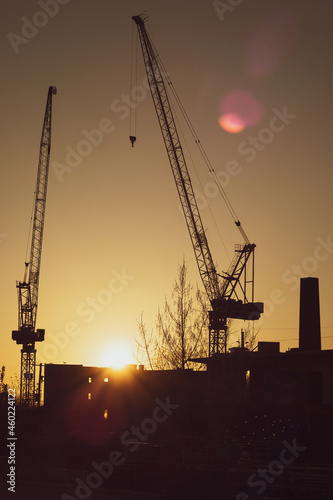 Silhouette of Two Industrial Construction Cranes at Sunset with Lens Flare