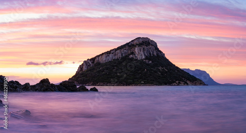 Stunning view of Figarolo island during a romantic and relaxing sunrise reflected on a calm water flowing in the foreground. Golfo Aranci, Sardinia, Italy.