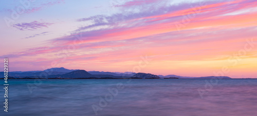 Stunning seascape with a romantic and relaxing sunrise reflected on a calm water flowing in the foreground. Golfo Aranci, Sardinia, Italy.