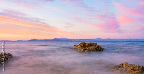 Stunning seascape with a romantic and relaxing sunrise reflected on a calm water flowing in the foreground. Golfo Aranci, Sardinia, Italy.
