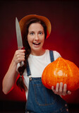 Female gardener aggressively carves a lantern out of a pumpkin with a knife for a horror holiday. Concept of Halloween.