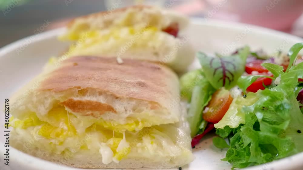 Close-Up of Sandwich Bread with Egg Filling and Fresh Green Salad on White Plate. Breakfast in Cafe or Restaurant. Fast food Serving. Delicious Roasted Soft Bun with Cheese and Egg. Lunch Snack Close-Up of Sandwich Bread with Egg Filling and Fresh Green Salad on White Plate. Breakfast in Cafe or Restaurant. Fast food Serving. Delicious Roasted Soft Bun with Cheese and Egg. Lunch Snack