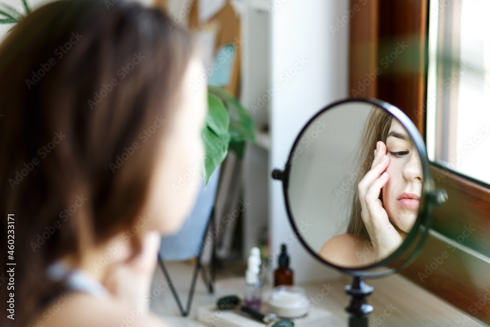 Beauty girl looking at mirror while touching her face and applying cream, wrinkles during morning beauty routine. Happy smiling beautiful young woman applying moisturizer lotion . Beauty girl looking at mirror while touching her face and applying cream, wrinkles during morning beauty routine. Happy smiling beautiful young woman applying moisturizer lotion .