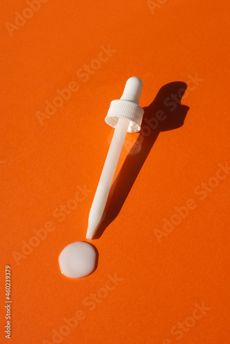 Open cap with dropper pipette with serum. Orange background with daylight and the appearance of the texture of the cream. Skincare products , natural cosmetic. Beauty concept for face and body care