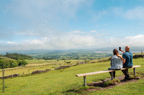 Father and daughter spend time together on a bench in a park with great scenery view Bald father and teenager girl outdoors. One parent or divorced family concept. Warm sunny day, cloudy sky. © mark_gusev