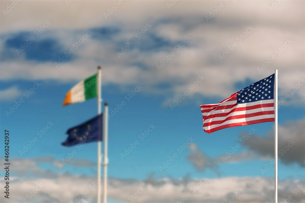 Waving flag of United States of America against pastel light blue color sky in focus. National flag of Ireland and Euro Union out of focus