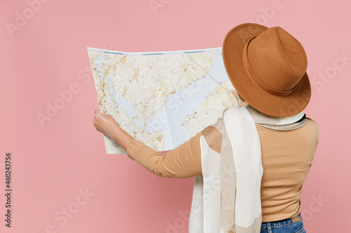 Back rear view traveler tourist elderly senior woman 55 years old wear brown shirt hat scarf hold examine read map search place direction isolated plain pastel light pink background studio portrait