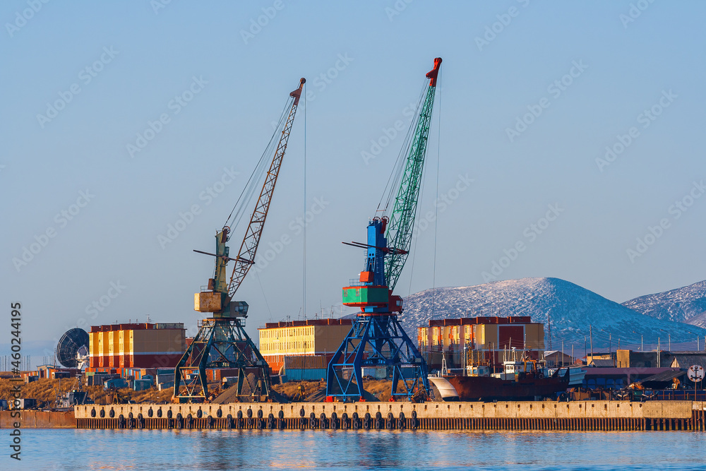 Cargo seaport and coastal settlement in the Russian Far North in the Arctic. View of the pier, cranes in the port, colorful buildings and mountains. Tavayvaam, Chukotka, Siberia, Far East of Russia.