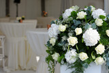 White roses in flower arrangement for a reception with defocussed tables with white napkins